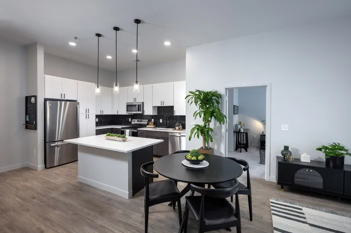 The Elex Apartments - Modern kitchen with sleek cabinetry, stainless steel appliances, and elegant island lighting, adjacent to a chic dining area with lush greenery for a fresh, inviting atmosphere.