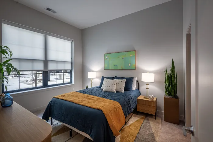 The Elex Apartments - Inviting bedroom with modern decor, featuring a large window with soft lighting, a cozy bed with stylish pillows, and elegant nightstands, creating a serene and comfortable living space.