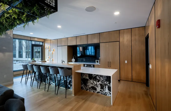 The Elex Apartments - Luxurious modern kitchen with sleek wooden cabinetry, expansive island seating, and chic marble accents beneath bright pendant lighting.