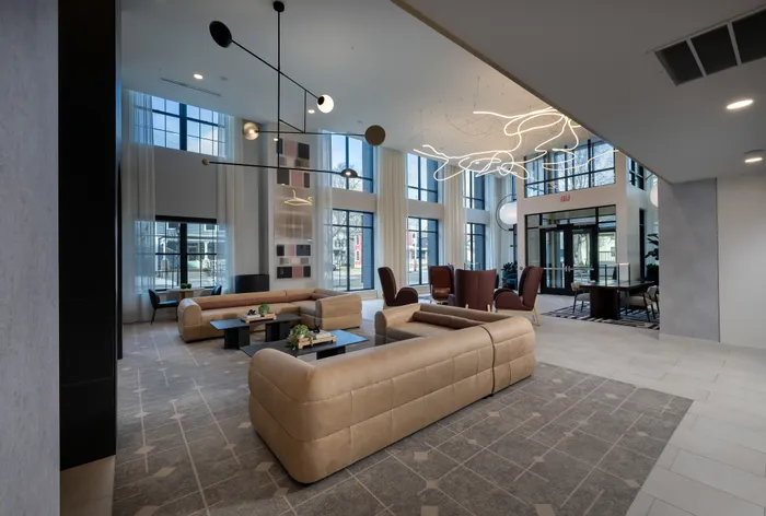 The Elex Apartments - Elegant lobby with modern lighting, cozy beige sectional sofas, and floor-to-ceiling windows for natural light.