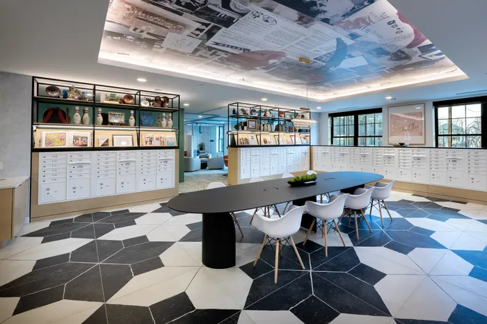 The Elex Apartments - Chic modern lobby with a long black table, white chairs, artistic ceiling mural, and abundant shelving displaying books and decor.