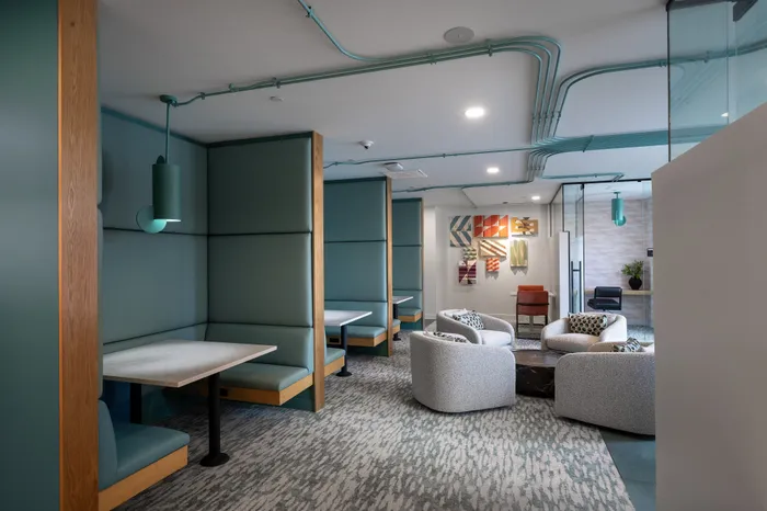 The Elex Apartments - Modern lounge area with sleek teal booths and plush seating, perfect for relaxation and meetings, accented by stylish art pieces and ambient lighting.