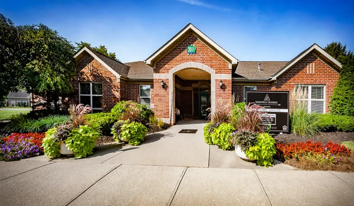 Inviting brick apartment welcome center with charming landscape and vibrant flowers, showcasing community warmth.