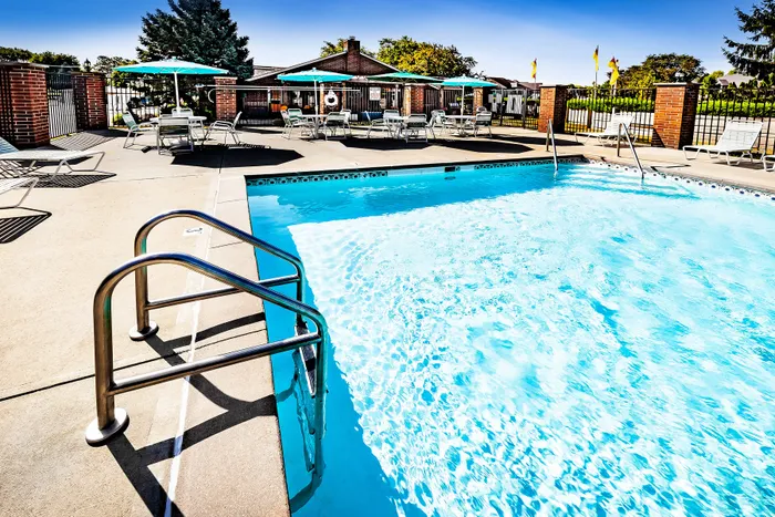 Inviting outdoor swimming pool with modern lounge chairs and vibrant umbrellas, offering a perfect relaxation spot in a serene community setting.