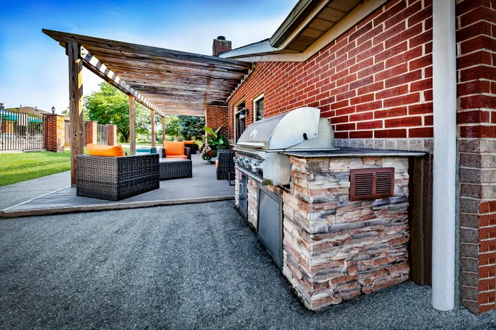 Chic outdoor patio featuring a modern barbecue grill, elegant wicker furniture, and stylish brickwork.