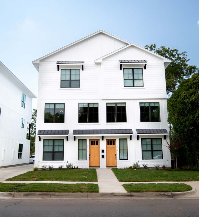 Charming modern apartment building with white exterior, large windows, and manicured lawn against a clear blue sky.