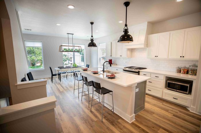 Elegant, modern kitchen and dining space with bright natural lighting, featuring a stylish island with bar stools, sleek cabinetry, and hardwood flooring.