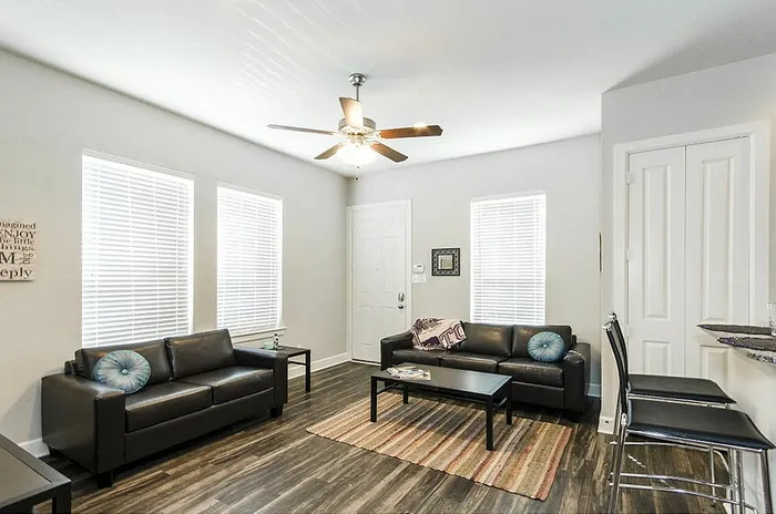 Bright and inviting living room featuring elegant leather sofas, modern coffee table, and sleek ceiling fan, perfect for relaxation and entertaining.