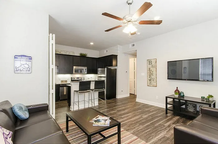 Bright, modern living room with sleek dark wood floors, featuring a comfortable leather sofa, stylish kitchen with stainless steel appliances, and cozy bar seating.
