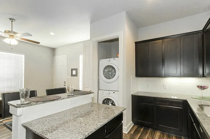 Modern kitchen with sleek dark cabinets, sparkling granite countertops, and in-unit washer and dryer for convenience and style.