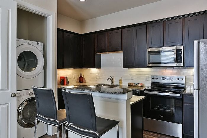 Modern kitchen with sleek dark cabinetry, stainless steel appliances, and an in-unit washer and dryer for convenience.