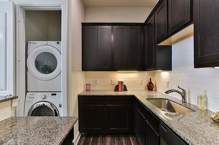 Modern kitchen with sleek dark wood cabinets, granite countertops, and a convenient in-unit laundry tucked neatly into a compact space.