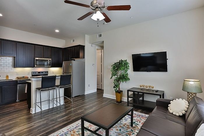 Modern living space with sleek kitchen, cozy seating area, and stylish decor, accentuated by dark wood flooring and elegant lighting.