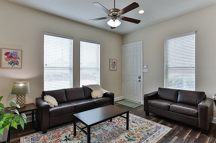 Bright and cozy living room with elegant leather sofas, decorative rug, and inviting natural light through large windows.