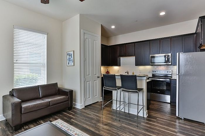 Modern open-concept kitchen and living area featuring sleek dark wood cabinets, stainless steel appliances, and cozy seating.