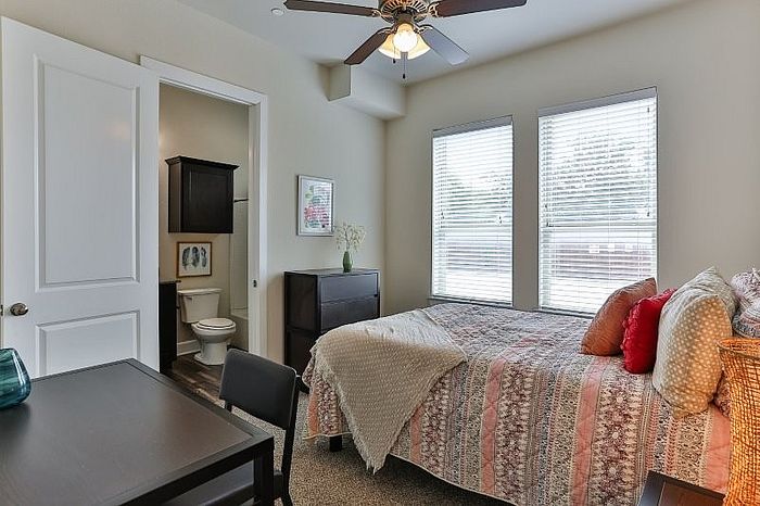 Cozy bedroom with elegant decor, featuring a comfortable bed, chic furnishings, and ample natural light through large windows.