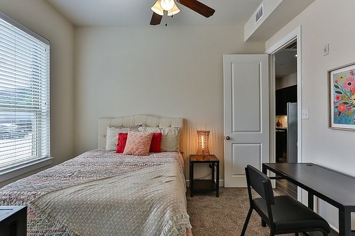 Cozy bedroom with a comfortable bed adorned with decorative pillows, warm ambient lighting, and a study desk, ideal for relaxation and productivity.