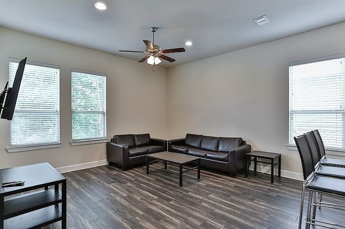Bright and spacious living room with sleek wooden floors, modern ceiling fan, and stylish leather sofas offering a cozy atmosphere.