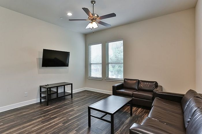 Inviting living room with modern leather couches, sleek hardwood floors, and a wall-mounted TV, perfect for relaxation.