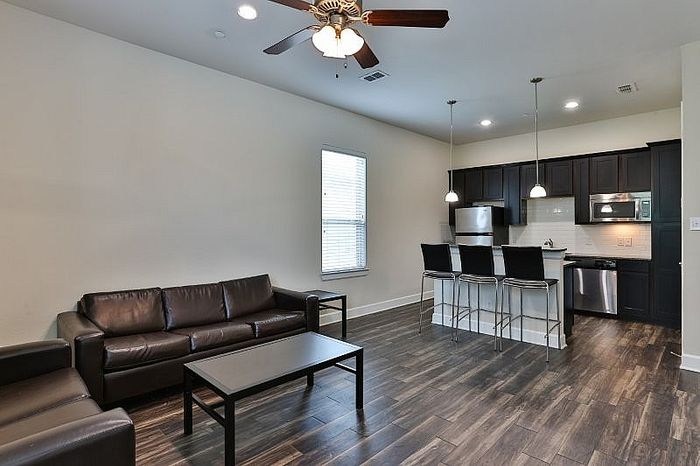 Modern open-concept living space with sleek dark wood flooring, stylish kitchen with stainless steel appliances and elegant lighting, complemented by comfortable leather seating.