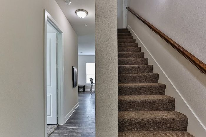 Contemporary hallway with elegant staircase and inviting view of a bright dining area, showcasing modern interior design.
