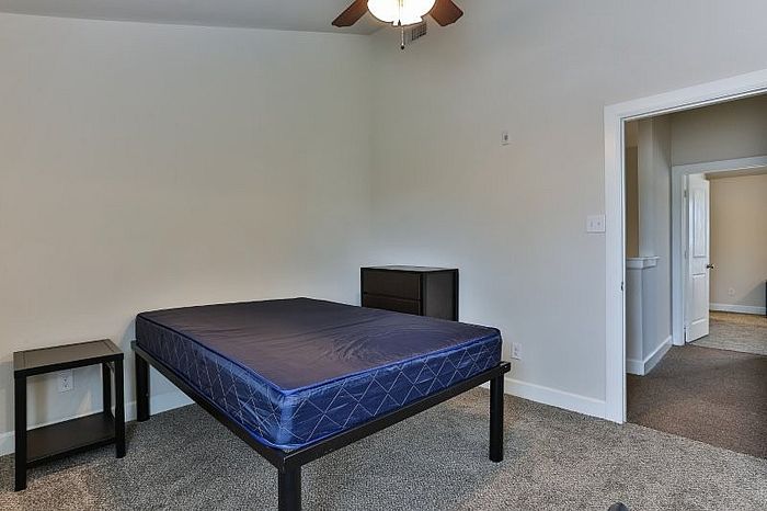 Inviting bedroom with plush carpeting, ceiling fan, and ample natural light, featuring a comfortable bed and modern furniture.