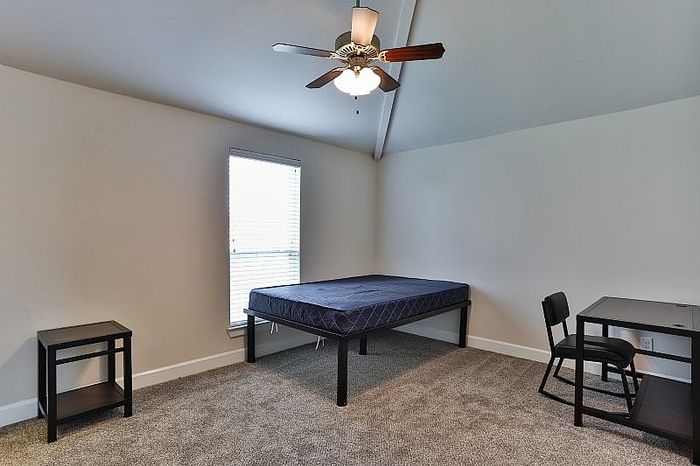 Bright and airy bedroom with high ceilings, featuring a modern fan, cozy carpeted flooring, and ample natural light from a large window.