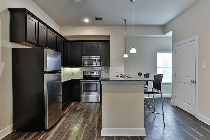 Modern kitchen with sleek dark cabinets, stainless steel appliances, and a stylish breakfast bar with pendant lighting.