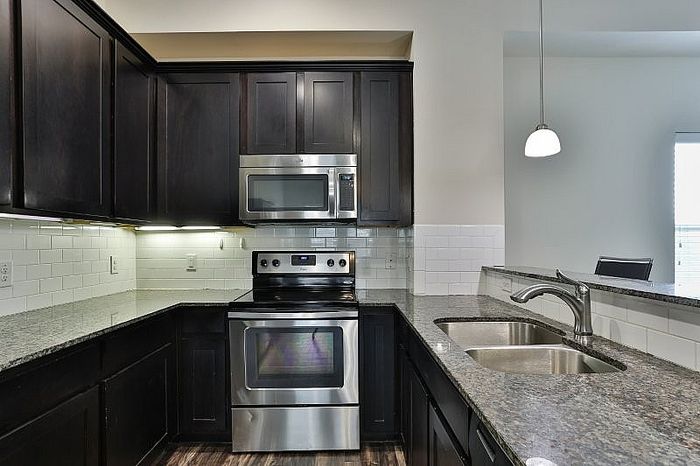 Modern kitchen with sleek dark cabinetry, stainless steel appliances, granite countertops, and elegant pendant lighting.