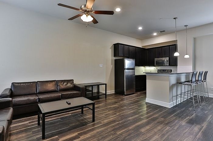 Contemporary open-plan living room with sleek dark wood flooring, cozy leather sofas, and a modern kitchen featuring stainless steel appliances and stylish bar seating.