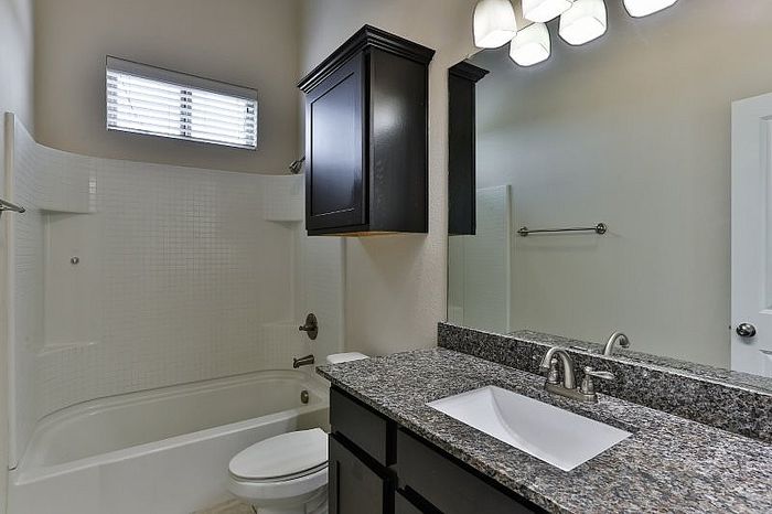Elegant bathroom with modern fixtures, granite countertop, and ample natural light, featuring a sleek bathtub and stylish dark cabinet.