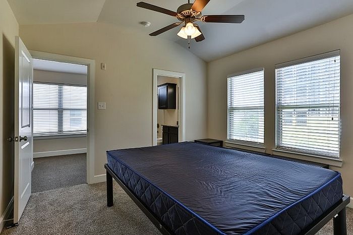 Bright and airy bedroom featuring large windows, plush carpeting, and an elegant ceiling fan for optimal comfort.