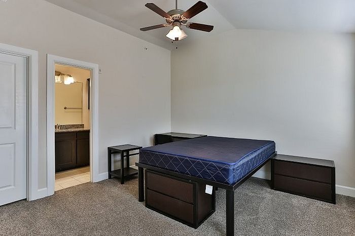 Spacious bedroom with plush carpeting, modern ceiling fan, and a private en-suite bathroom.