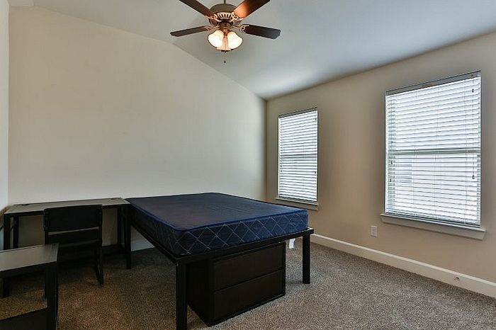 Bright and spacious bedroom with large windows, a cozy bed, stylish ceiling fan, and sleek workspace creating a perfect retreat.