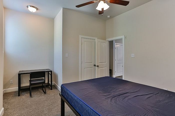 Inviting bedroom with cozy carpet, ceiling fan, and a convenient study desk, perfect for relaxation and productivity.