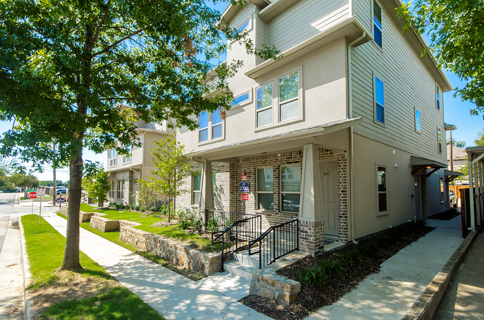 Charming townhouse exterior with modern design and lush landscaping on a sunny day.