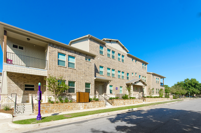 Charming apartment complex with modern brick facade, inviting balconies, and lush landscaping under a clear blue sky.