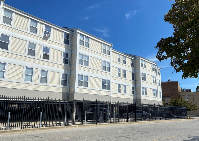 Modern four-story apartment building with beige siding and large windows.