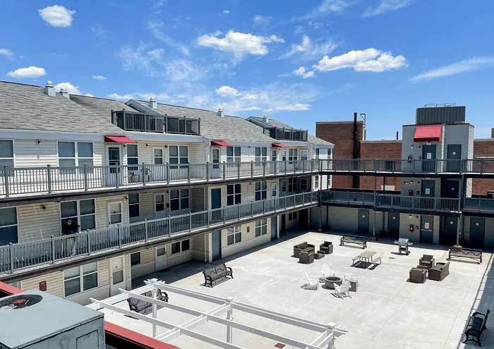 Sunny courtyard view of a modern apartment complex with balconies and seating area.