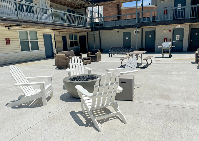 Inviting courtyard with Adirondack chairs around a modern fire pit, surrounded by cozy seating and a grill.
