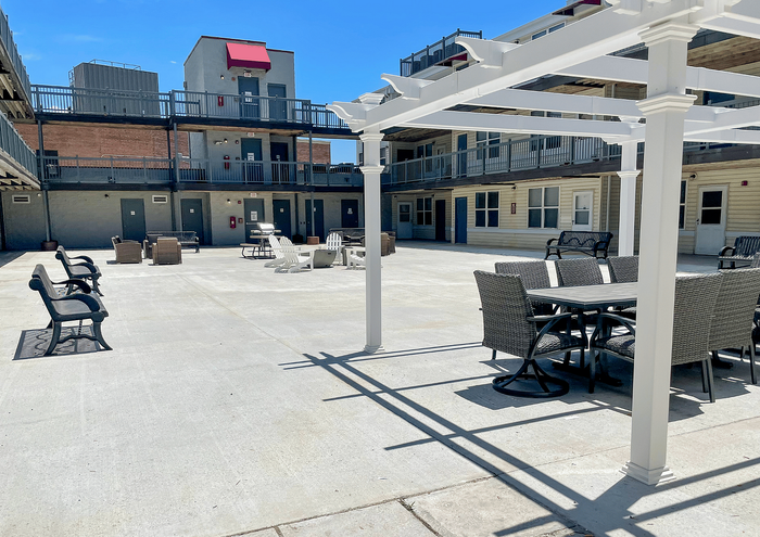 Sunlit courtyard featuring seating areas, a pergola, and modern apartment balconies.