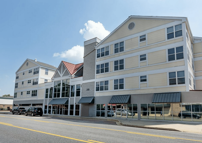 Modern four-story apartment building with large windows and retail spaces on the ground floor.
