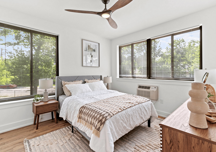 Elegant bedroom with large windows, modern furniture, and a ceiling fan, filled with natural light.