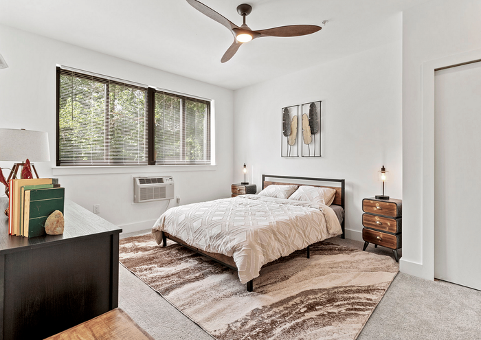 Bright bedroom with stylish decor, featuring a cozy bed, modern ceiling fan, and large window with greenery view.