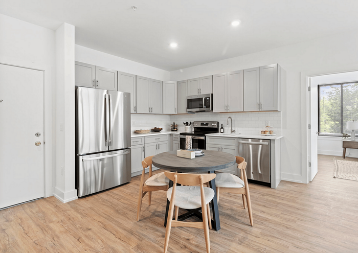 Bright kitchen with stainless steel appliances, modern cabinetry, and round wooden dining table with chairs.