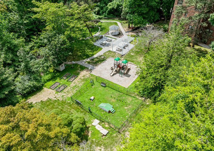 Aerial view of a community park featuring a playground, garden, and walking paths surrounded by trees.