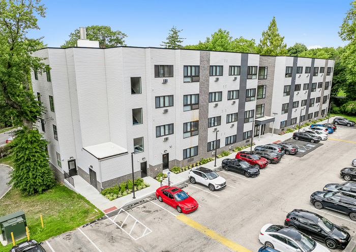 Modern four-story apartment building with landscaped surroundings and ample parking.