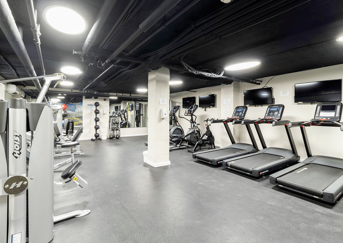 Modern fitness center equipped with treadmills, exercise machines, and wall-mounted TVs.