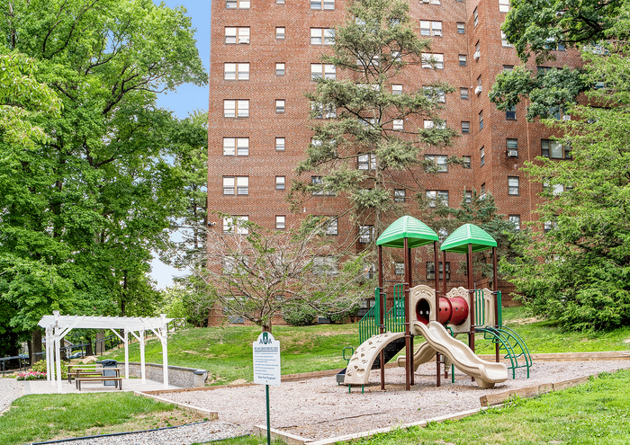 Charming apartment complex with brick building, lush trees, and a vibrant children's playground.