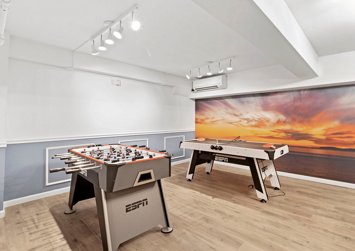 Modern game room featuring a foosball table and air hockey against a sunset mural backdrop.